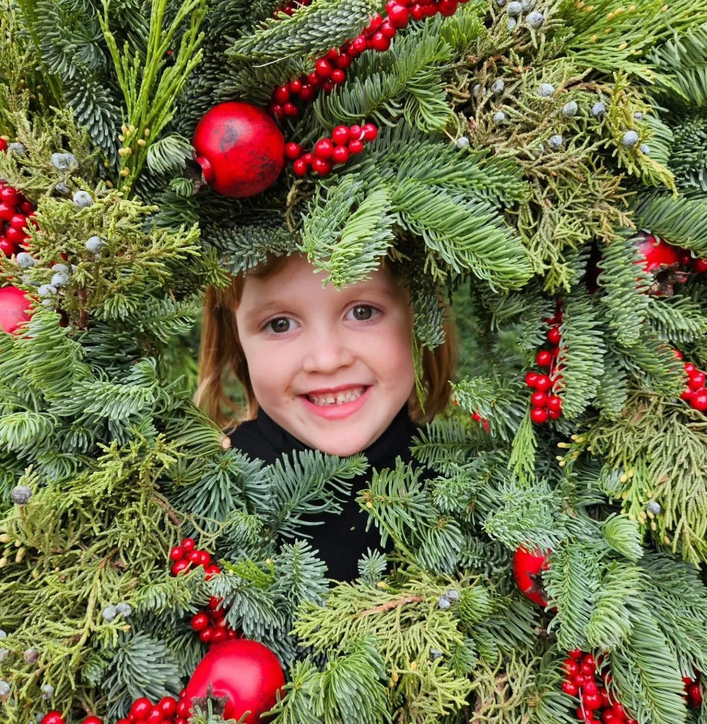 Child peeking through a festive wreath at Noel's Tree Farm
