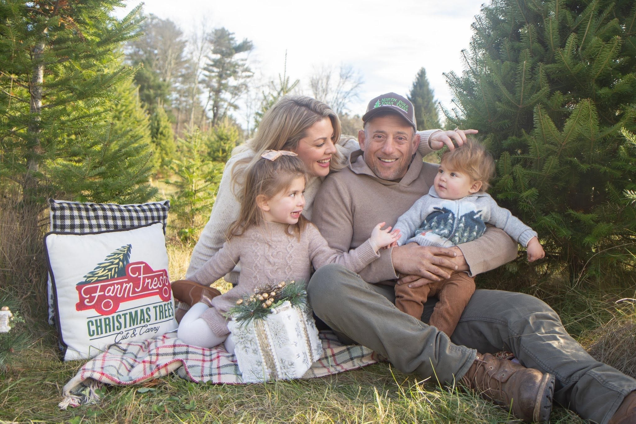 Family of four sitting among Christmas trees at the farm